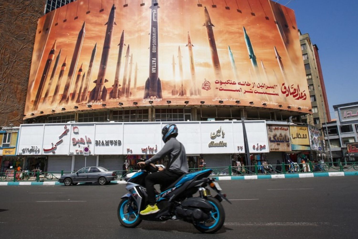 Un uomo passa in moto davanti a un cartellone pubblicitario che raffigura missili balistici iraniani in servizio a Teheran il 19 aprile 2024. I media statali iraniani hanno riferito di esplosioni nella provincia centrale di Isfahan