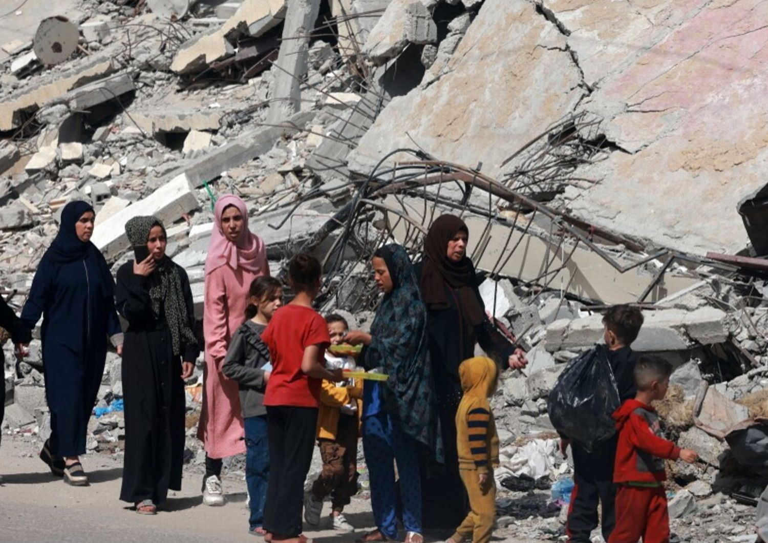 Donne e bambini palestinesi camminano vicino a un edificio distrutto da un bombardamento israeliano a Rafah, nel sud della Striscia di Gaza, il 31 marzo 2024