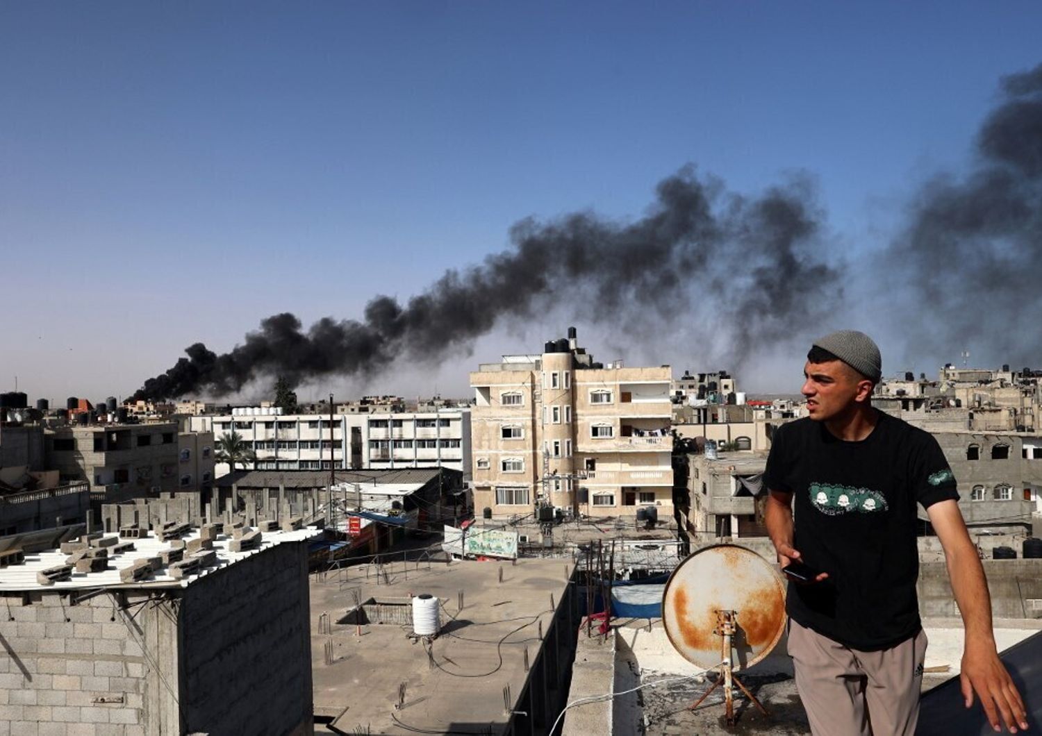Un uomo osserva il fumo nero e denso che si leva dall'incendio di un edificio causato dai bombardamenti israeliani a Rafah, nel sud della Striscia di Gaza, il 10 maggio 2024