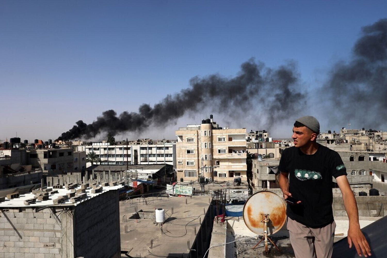 Un uomo osserva il fumo nero e denso che si leva dall'incendio di un edificio causato dai bombardamenti israeliani a Rafah, nel sud della Striscia di Gaza, il 10 maggio 2024