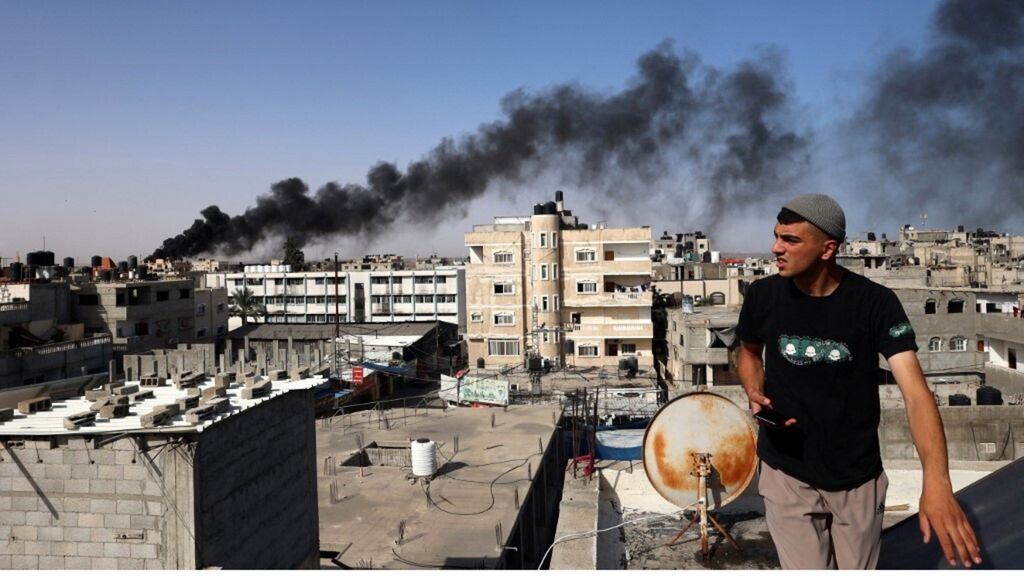 Un uomo osserva il fumo nero e denso che si leva dall'incendio di un edificio causato dai bombardamenti israeliani a Rafah, nel sud della Striscia di Gaza