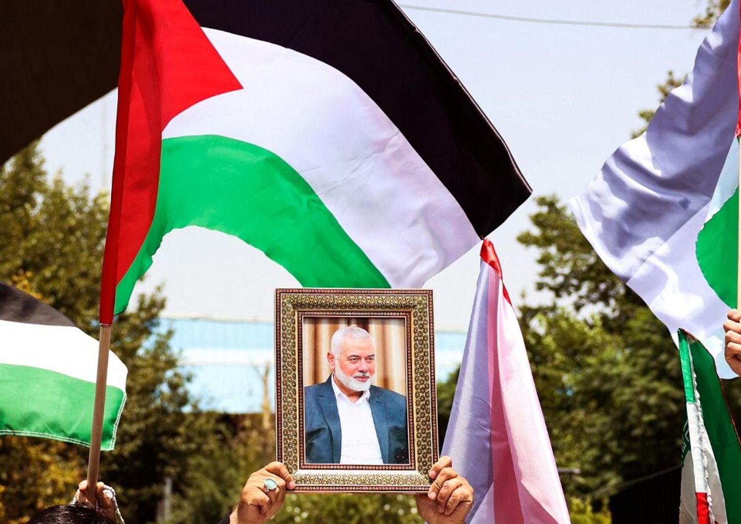 Persone reggono la bandiera palestinese e un ritratto del capo di Hamas Ismail Haniyeh, assassinato, durante una manifestazione all'Università di Teheran, nella capitale iraniana Teheran, il 31 luglio 2024, mentre l'Iran dichiara tre giorni di lutto