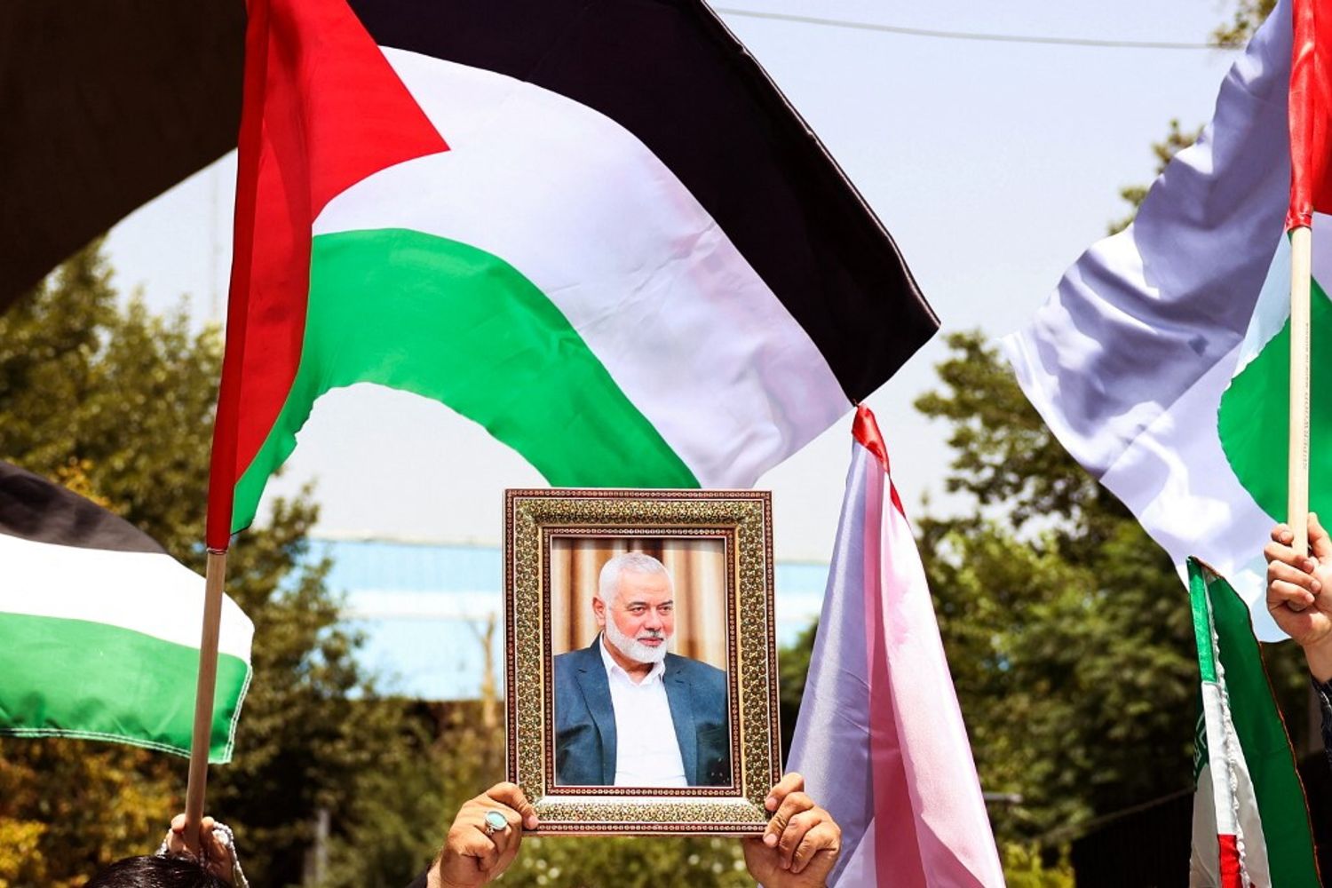 Persone reggono la bandiera palestinese e un ritratto del capo di Hamas Ismail Haniyeh, assassinato, durante una manifestazione all'Università di Teheran, nella capitale iraniana Teheran, il 31 luglio 2024, mentre l'Iran dichiara tre giorni di lutto