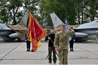 Il presidente ucraino Zelensky consegna le insegne di una bandiera a un militare mentre si trova di fronte a una coppia di caccia F16 durante una cerimonia tenuta in occasione della Giornata delle forze aeree ucraine il 4 agosto 2024