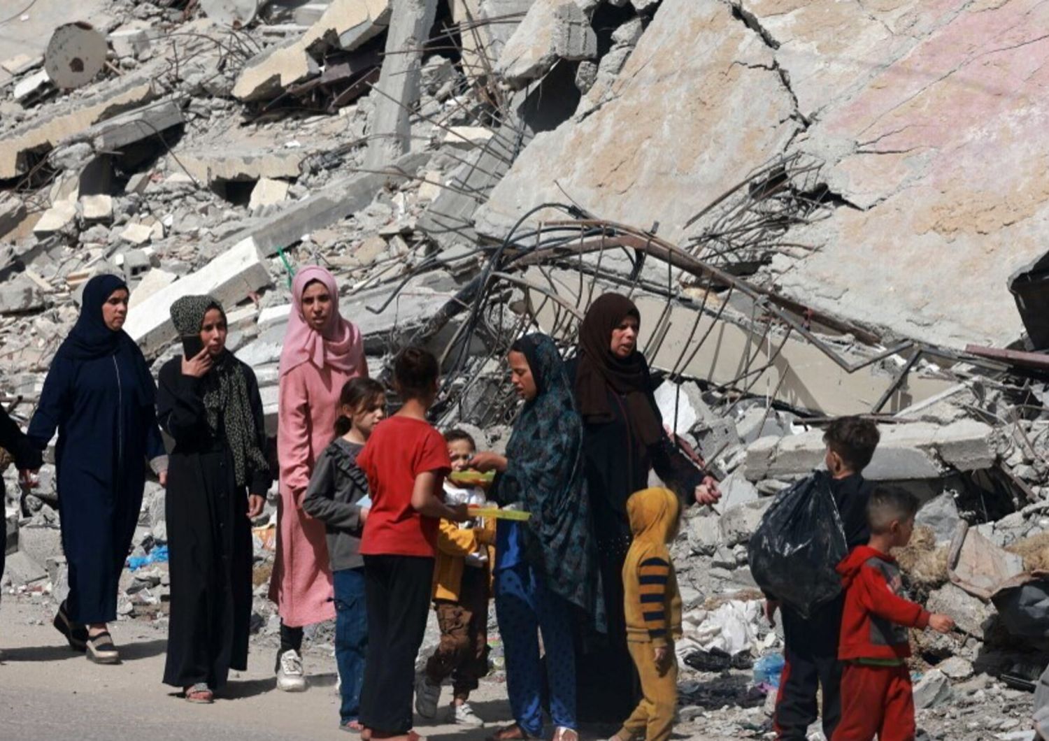 Donne e bambini palestinesi camminano vicino a un edificio distrutto da un bombardamento israeliano a Rafah, nel sud della Striscia di Gaza, il 31 marzo 2024