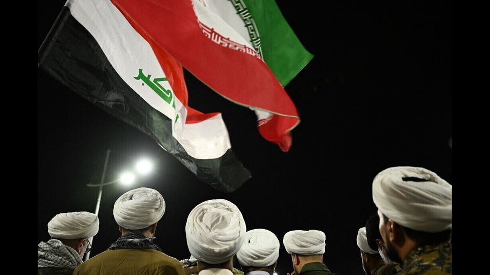 Religiosi musulmani sciiti in tenuta militare sventolano bandiere iraniane (R) e irachene durante una manifestazione tenutasi sul lungomare di Shatt al-Arab nella città meridionale irachena di Bassora per protestare contro gli attacchi di Israele contro l'Iran.