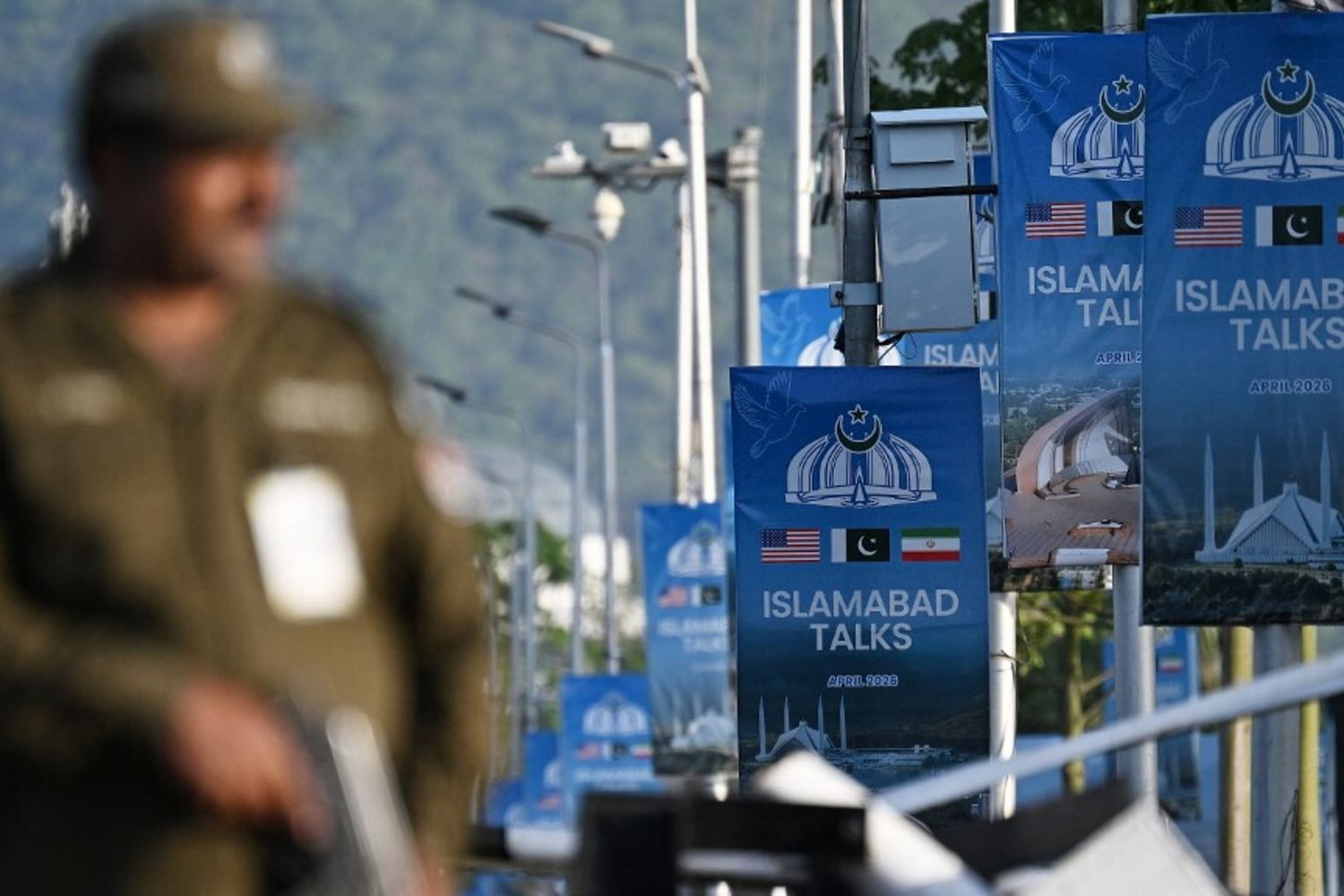 Un agente di polizia monta la guardia accanto a dei manifesti che evidenziano la mediazione del Pakistan nei colloqui di pace tra Iran e Stati Uniti