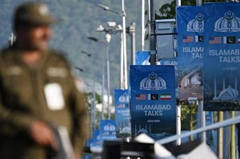 Un agente di polizia monta la guardia accanto a dei manifesti che evidenziano la mediazione del Pakistan nei colloqui di pace tra Iran e Stati Uniti
