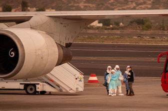 Alcune persone indossano tute protettive e si imbarcano a Tenerife su un aereo diretto negli Stati Uniti con a bordo i passeggeri evacuati dalla nave da crociera MV Hondius – immagine del 10 maggio 2026