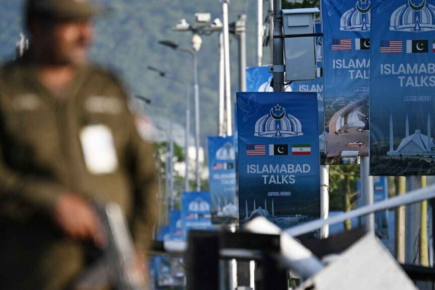 Un agente di polizia monta la guardia accanto a dei manifesti che evidenziano la mediazione del Pakistan nei colloqui di pace tra Iran e Stati Uniti