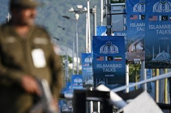 Un agente di polizia monta la guardia accanto a dei manifesti che evidenziano la mediazione del Pakistan nei colloqui di pace tra Iran e Stati Uniti