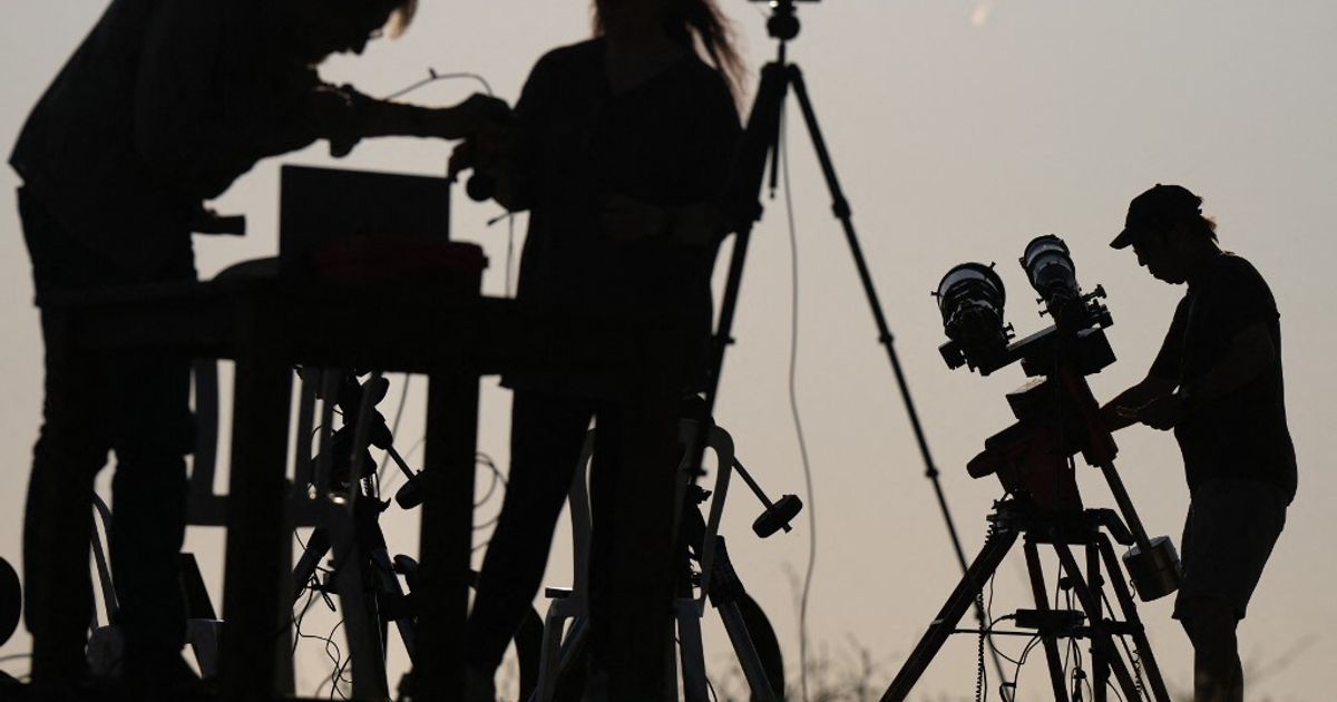 Un gruppo di persone osserva l’eclissi solare in un’area aperta, mentre un’altra persona guarda un telefono con preoccupazione