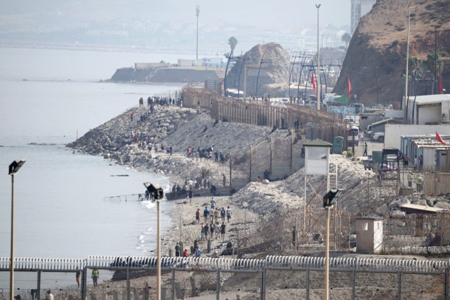 Migranti camminano lungo la costa vicino alla recinzione di confine che separa il Marocco dall'enclave spagnola di Ceuta