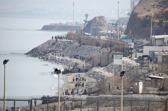 Migranti camminano lungo la costa vicino alla recinzione di confine che separa il Marocco dall'enclave spagnola di Ceuta