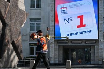 Un uomo con un tosaerba passa davanti a uno schermo digitale sull'edificio della sede del partito Russia Unita, che invita i cittadini a votare per i candidati del partito alle prossime elezioni per la Duma di Stato